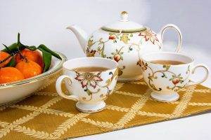 Use the good stuff including this floral teapot and two tea-filled cups next to a bowl of madarins