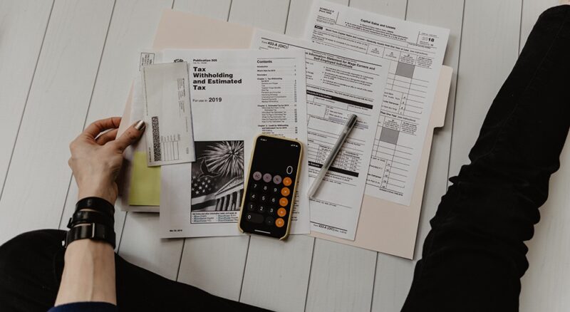 Tax, other paperwork and a calculator are on the floor in front of someone sitting down out of shot