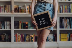 A woman holds a sign which says Read Good Books before a bookshelf. Time to declutter my bookshelf