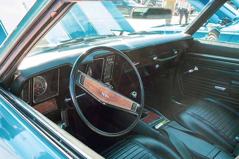 The neat, clean interior of a blue vintage car. The steering wheel has wooden panelling