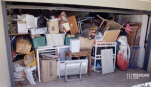 A overloaded garage with the door open. Boxes and furniture are piled and arranged up to the ceiling.