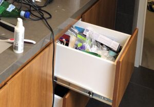 An open messy junk drawer contains boxes and plastic products