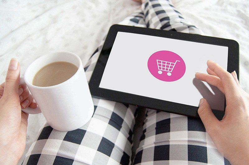 A hand holds a coffee and a tablet screen showing a shopping basket to signify consumerism and clutter