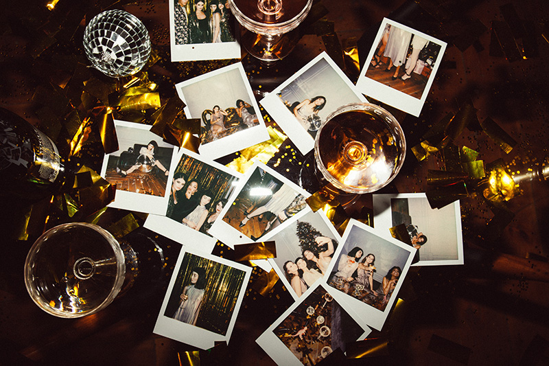 12 polaroid photos are scattered on a table amidst other mess, to show decluttering sentimental items