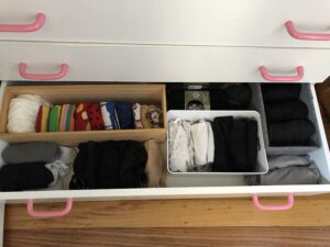 The bottom drawer is open to reveal smaller containers with folded socks. Decluttering and mental health