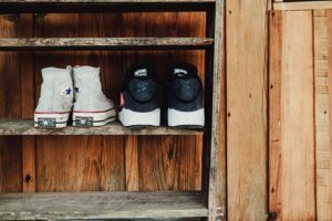 Two pairs of sneakers sit adjacent on an old timber shelf (shoe storage) in front of a timber wall