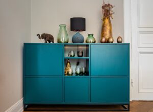 A bright blue transitional storage cupboard has various vases, a lamp and decorative items on top of it